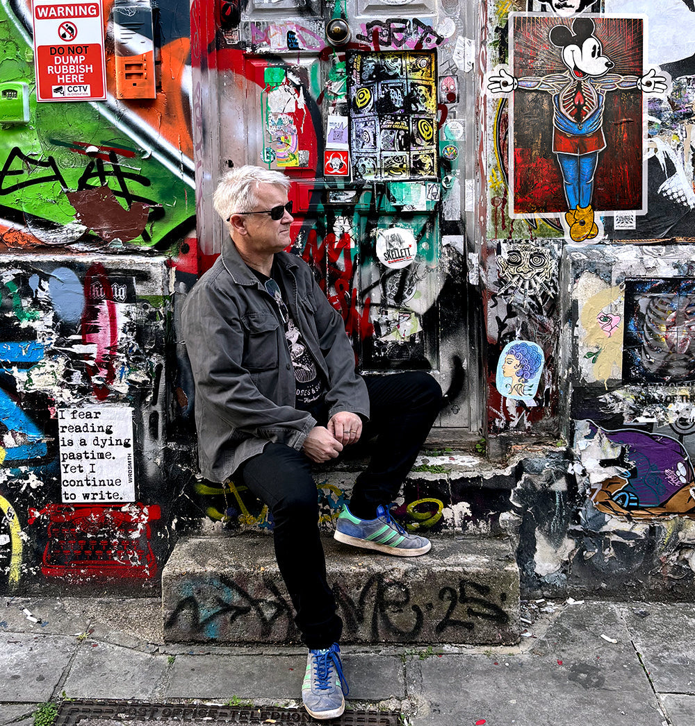 Paul sitting on a step in front of a wall of graffiti with Studio Skellett tag and artwork. London